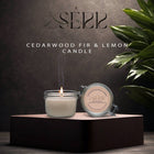 SerrBeauty Cedarwood, Fir & Lemon Beeswax Scented Candle in a glass jar with a lit wick, placed on a dark pedestal. The organic beeswax candle emits a soothing aroma with woodsy and citrus notes, perfect for home wellness and aromatherapy.