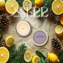 SerrBeauty Cedarwood, Fir & Lemon Beeswax Scented Candle 125 G in a round tin, surrounded by fresh lemons, fir branches, and pinecones. A natural, organic candle with a refreshing woodsy and citrus aroma.