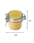 Unlit natural beeswax candle in a clear glass jar with a metal clasp, yellow label with black text, handmade, long burning, and wooden wick