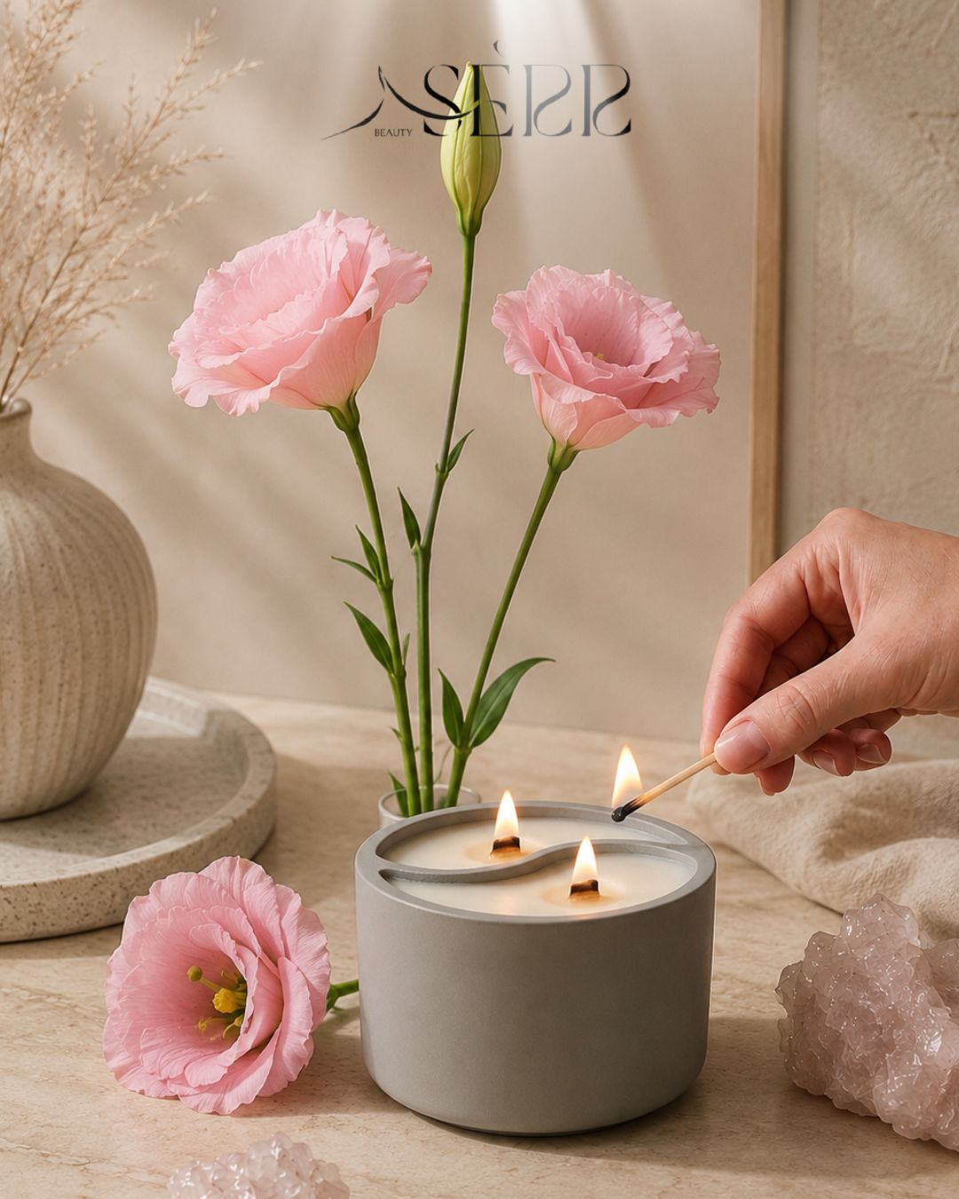 Gray concrete candle with wood wicks, surrounded by pink flowers, cozy home ambiance