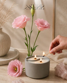 Gray concrete candle with wood wicks, surrounded by pink flowers, cozy home ambiance